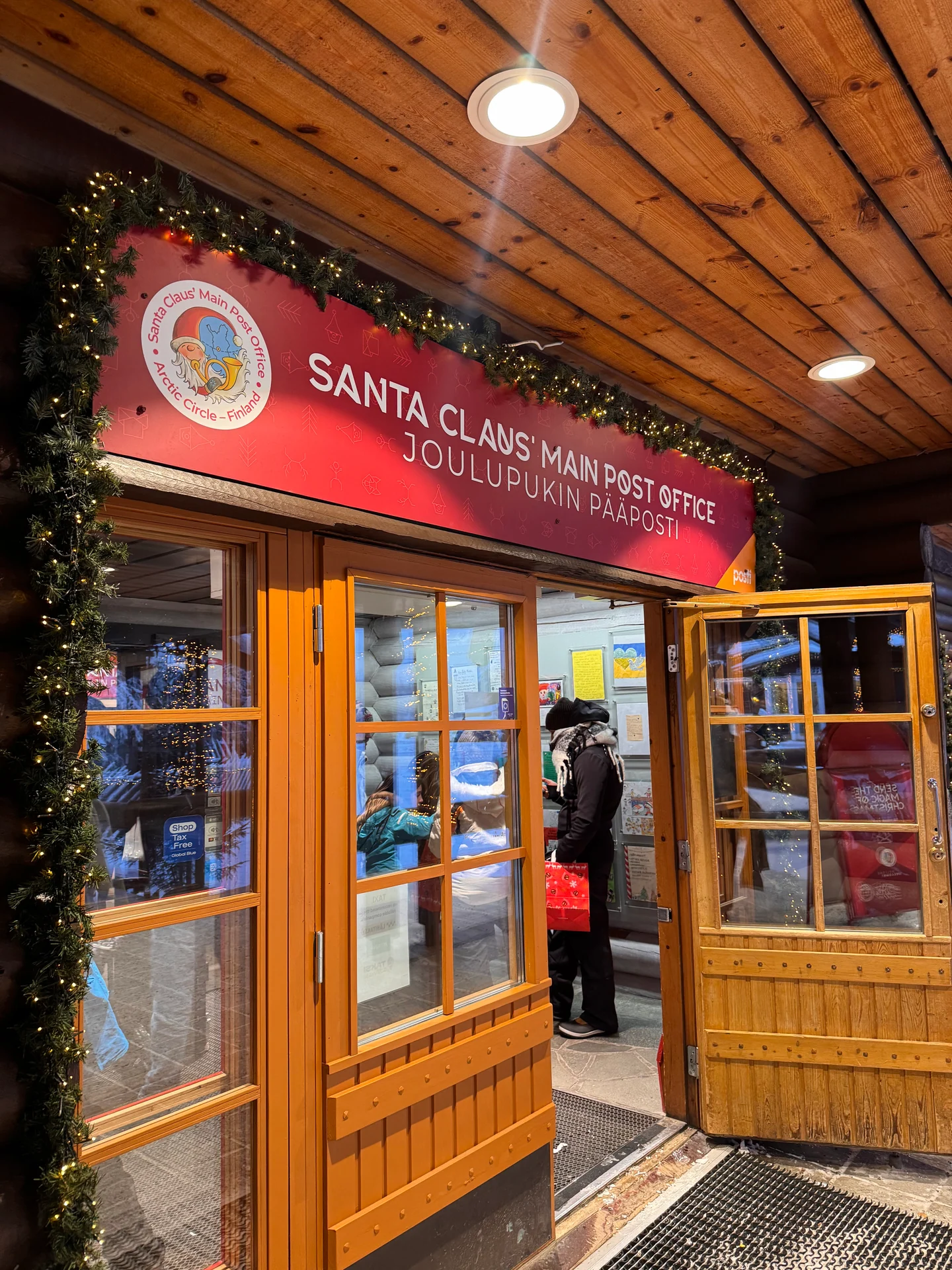 Entrance to Santa Claus Main Post Office with its red sign and wooden doors