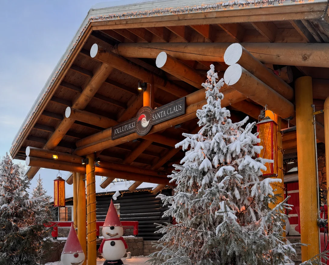 Snow-covered entrance to Santa Claus Office with Christmas trees and wooden beams
