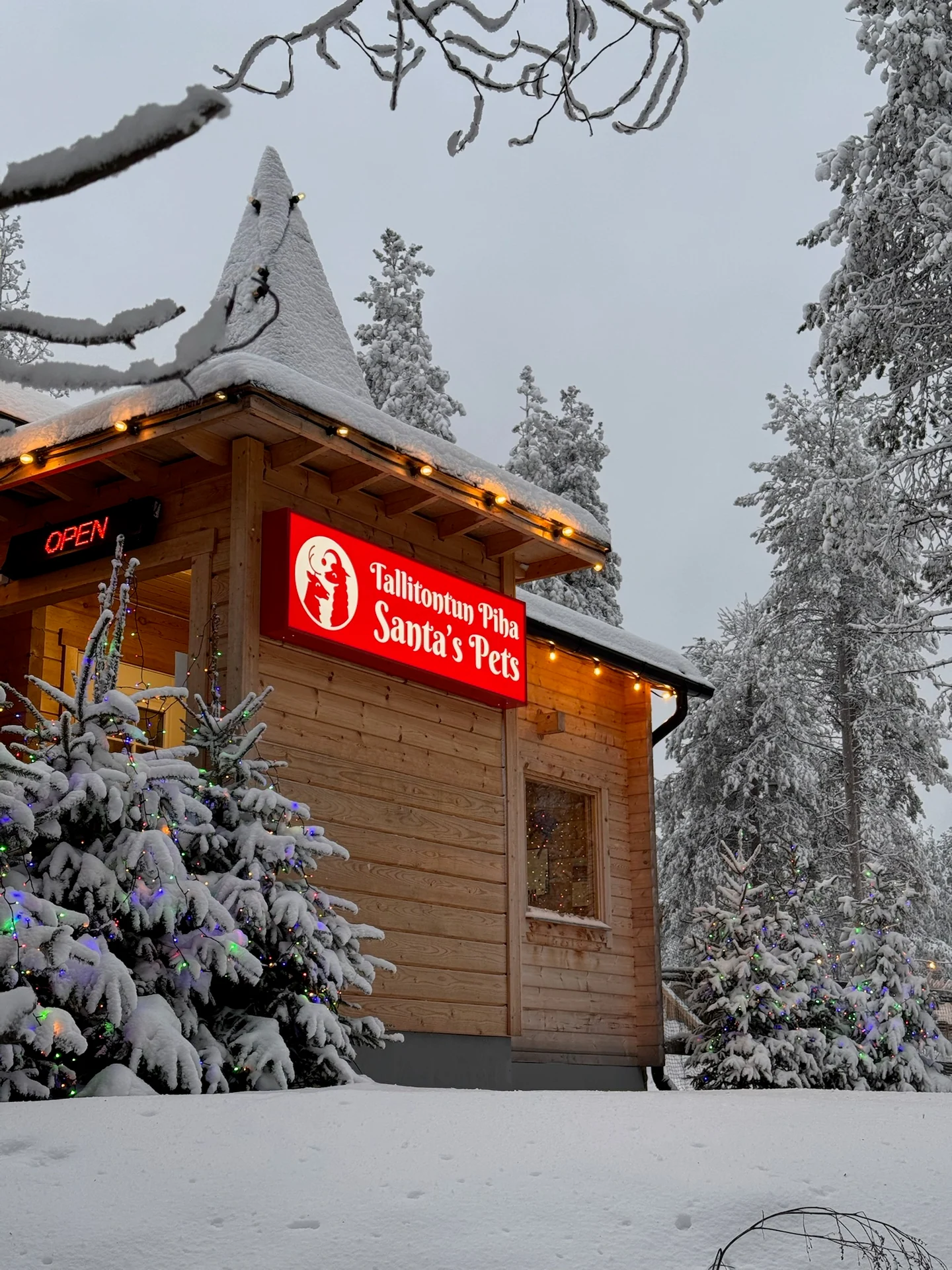 Snow-covered Santa's Pets entrance with a red sign and Christmas trees
